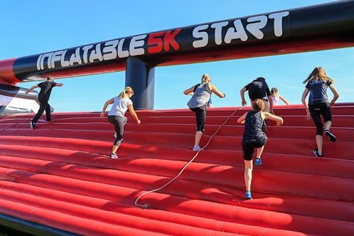 Fundraisers climbing red inflatable obstacle mountain