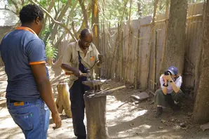 A farrier in a beige shirt hard at work outside in front of a photographer.