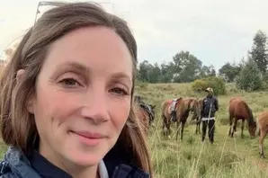 Kimberley Wells, Brooke's Senior Manager of Animal Welfare, pictured in a Brooke jacket while standing in front of horses in long grass
