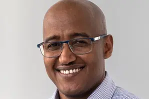 Aragie smiles while wearing a light blue shirt and glasses.