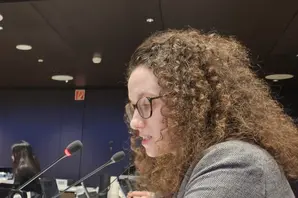 Ellie in a grey jumper sits at a desk in front of a microphone.