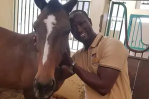Emmanuel stands with a brown horse, who has a white stripe down his face.