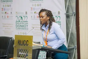 Brooke's Laura Kavata, wearing a blue shirt and trousers, stands over a podium as she speaks during a conference