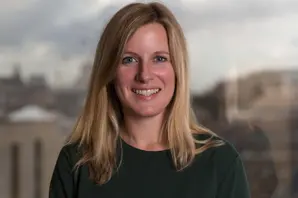 Dr Laura Skippen, wearing a navy blue t-shirt and Brooke sun hat, crouches down and makes friends with a donkey foal