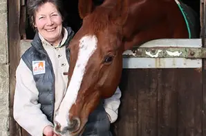 Brooke ambassador Jane Holderness-Roddam CVO CBE wears a Brooke gillet whilst stood with a brown horse in a stable