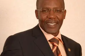 Eric Kimani smiles in a suit against a beige background