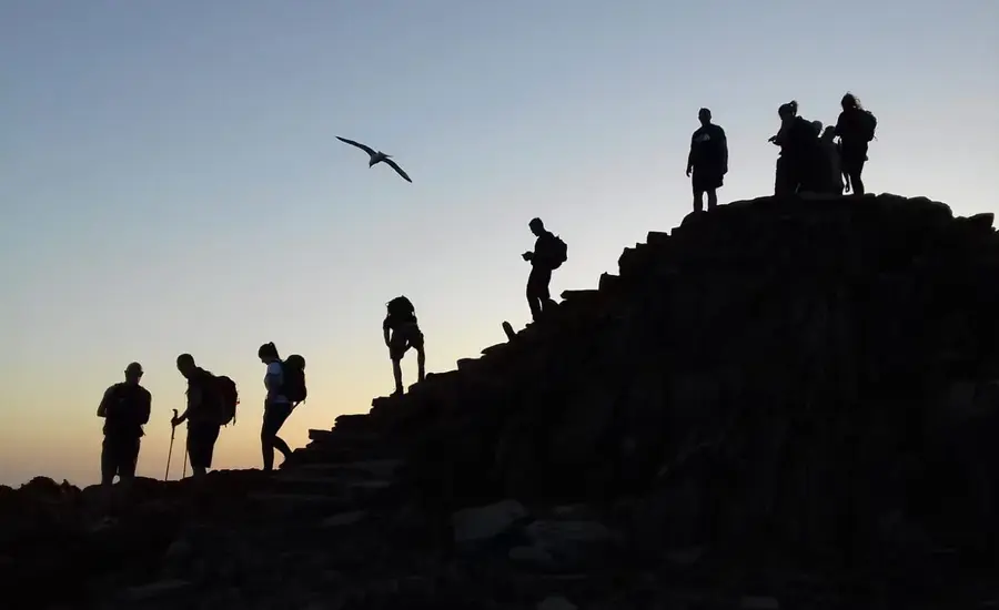 Hikers silhouetted at sunrise on Yr Wyddfa