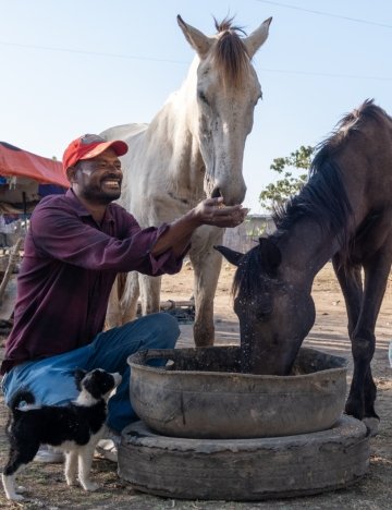 Tessema kneeling down and cupping water for his horse to drink from his hands.