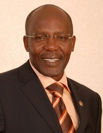Eric Kimani smiles in a suit against a beige backdrop