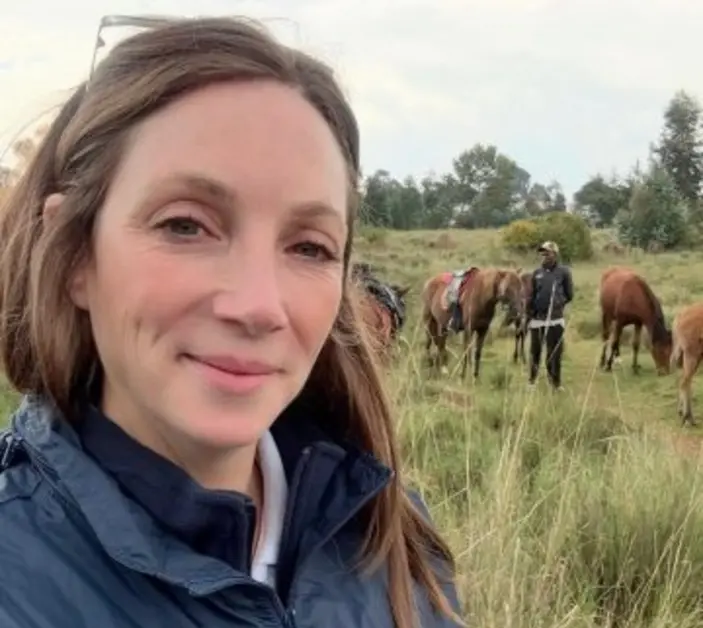 Kimberley Wells, Brooke's Senior Manager of Animal Welfare, pictured in a Brooke jacket while standing in front of horses in long grass
