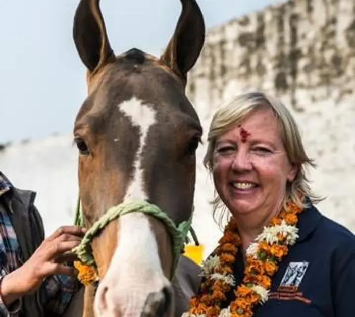 Deborah Meaden standing next to a horse while wearing a flower garment