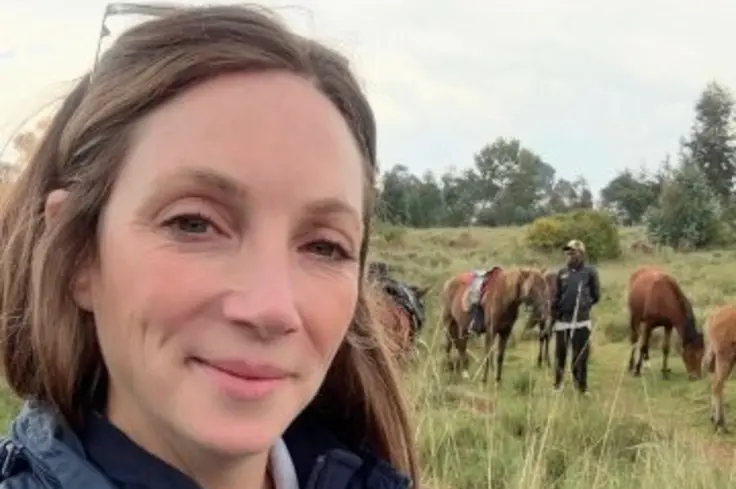 Kimberley Wells, Brooke's Senior Manager of Animal Welfare, pictured in a Brooke jacket while standing in front of horses in long grass