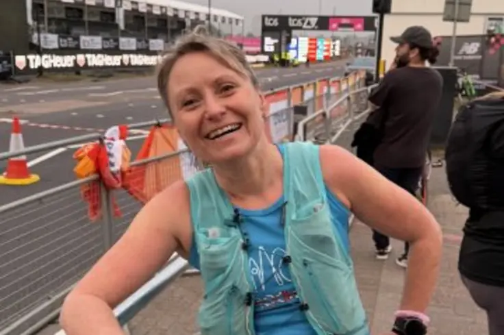 Kate leans on a barrier in blue running gear, resting after her reverse run.