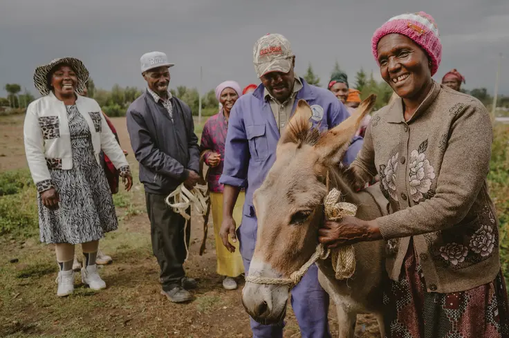 A group of people look happy whilst standing with a donkey, in Kenya